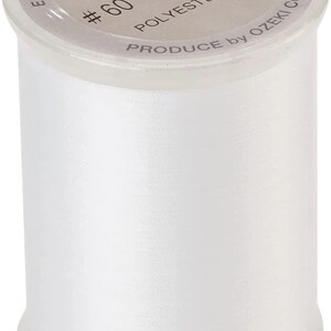 May include: A spool of white Brother embroidery bobbin thread. The label reads EMBROIDERY BOBBIN THREAD, brother, 1100m, #60, POLYESTER 100%, and PRODUCE by OZEKI CO., LTD. The spool is made of clear plastic and contains white polyester thread.