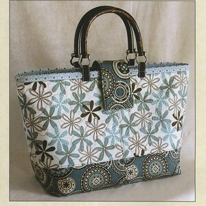 May include: A quilted tote bag featuring a white fabric with light blue and brown floral patterns, a dark teal base with circular motifs, and dark brown handles. The text Lazy Girl Designs #123 and Miranda Day Bag are visible on the page.