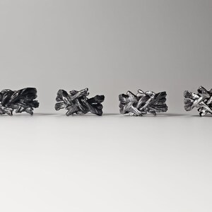 May include: Four silver rings with a unique, intricate, woven design. The rings are arranged in a row on a white surface.