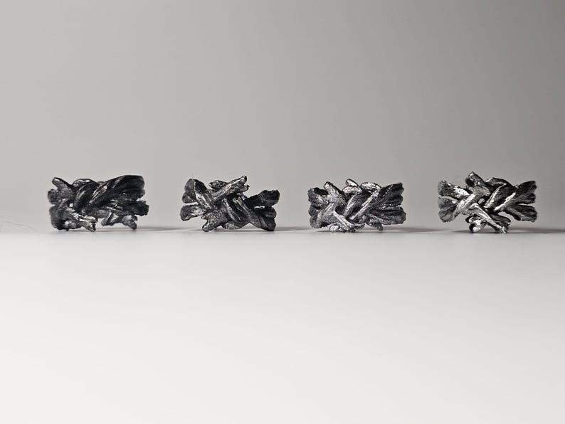 May include: Four silver rings with a unique, intricate, woven design. The rings are arranged in a row on a white surface.