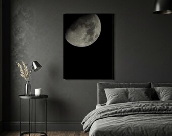 May include: A framed print of the moon in a bedroom setting. The moon is depicted in detail against a black background. The room has dark gray walls, a bed with gray bedding, and a small side table with a lamp and vase.