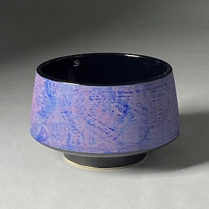 May include: A small, black and purple ceramic bowl with a flared rim and a wide base. The bowl has a textured, marbled design.
