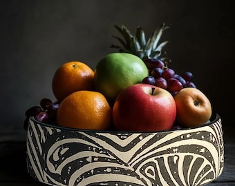 May include: A decorative fruit bowl filled with fresh fruit. The bowl has a black and white zebra stripe pattern. The fruit includes oranges, a green apple, a red apple, grapes, and a pineapple.