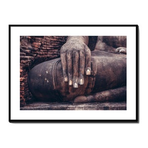 May include: Close-up of a weathered stone Buddha statue with a hand resting on its lap. The statue is in a seated meditation pose, and the hand is partially covered by the folds of the robe. The fingers are long and slender, and the nails are worn and chipped.