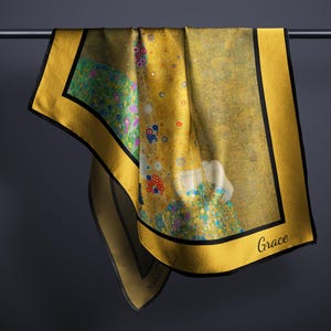 May include: A yellow silk scarf with a black border and a colorful painting of a couple embracing. The scarf has the word "Grace" printed in black on the bottom right corner.