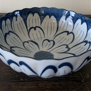 May include: A white ceramic bowl with a blue floral design. The bowl has a scalloped edge and a wavy design around the bottom.