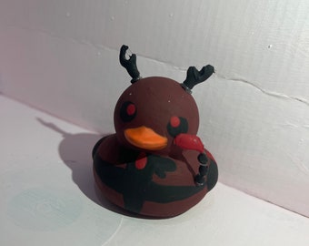 May include: A brown rubber duck with black antlers, red eyes, and black and red stripes. The duck is painted with a black and red design.