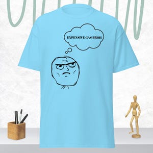 Puede incluir: Camiseta azul claro con una cara estilo meme y una burbuja de pensamiento. La burbuja de pensamiento contiene el texto "EXPENSIVE GAS BROH". El texto y la cara son negros.