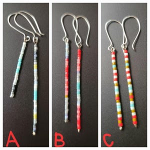 Puede incluir: Tres pares de pendientes de cuentas con ganchos plateados. Los pendientes presentan cuentas de colores en filas verticales. Un par tiene cuentas turquesas, blancas y negras. Otro tiene cuentas rojas, rosas y blancas. El tercer par tiene cuentas rojas, blancas, amarillas y turquesas.