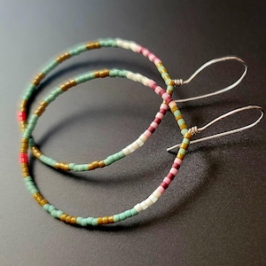 Puede incluir: Un par de pendientes de aro con un diseño de cuentas. Los pendientes presentan una mezcla de colores, incluyendo verde, marrón, rosa, blanco y rojo. Los ganchos de los pendientes son de color plateado.