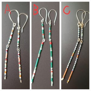 Puede incluir: Tres pares de pendientes colgantes con cuentas. Los pendientes presentan cuentas de colores en varios patrones. El primer par tiene una mezcla de colores, el segundo par tiene cuentas verdes, rojas y blancas, y el tercero tiene cuentas negras, blancas, naranjas y rojas.