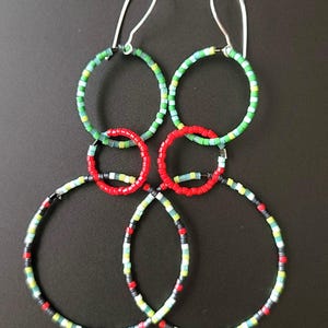 Puede incluir: Pendientes hechos a mano con un diseño único. Los pendientes están compuestos por múltiples aros de cuentas en verde, rojo y negro, con ganchos plateados. Las pequeñas y coloridas cuentas crean un efecto visual llamativo.
