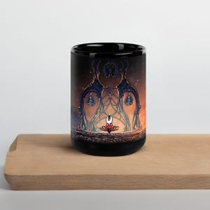 Puede incluir: Taza de cerámica negra con una ilustración de fantasía. La obra de arte representa una figura con atuendo rojo y blanco frente a una estructura ornamentada con un fondo de fuego. La taza está sobre una superficie de madera.