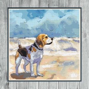 May include: A beagle dog stands on a sandy beach with a blue sky and white clouds in the background. The dog is looking to the right of the image.