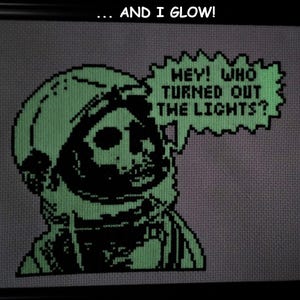 May include: A green and black cross-stitch design of a skeleton astronaut in a space helmet with the text "Hey! Who turned out the lights?" and the words "...and I glow!" at the top.