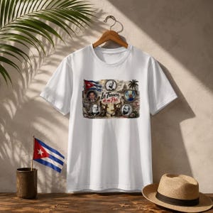Könnte beinhalten: Weißes T-Shirt mit einem grafischen Design mit der kubanischen Flagge, Porträts und dem Text "La Tranca de mi País". Das Design umfasst eine Flagge, Porträts und Palmen. Das T-Shirt hängt an einem Holzbügel.