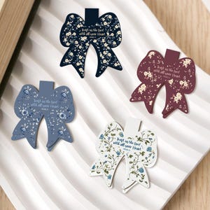 May include: Four bow-shaped bookmarks with floral patterns and the text "Trust in the Lord with all your Heart." The bookmarks are in navy, dusty blue, burgundy, and white, each with a different floral design.