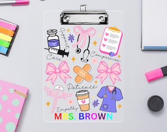 May include: A clear clipboard with a silver clip, featuring colorful medical-themed illustrations. Includes a syringe, stethoscope, pink bows, a coffee cup, and the name "MRS. BROWN" in rainbow colors. The clipboard is surrounded by office supplies.