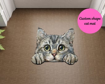 May include: A custom shape cat mat featuring a gray tabby kitten peeking out from behind a surface, with big green eyes and a cute expression. The mat is designed to look like the kitten is peeking out from behind something.