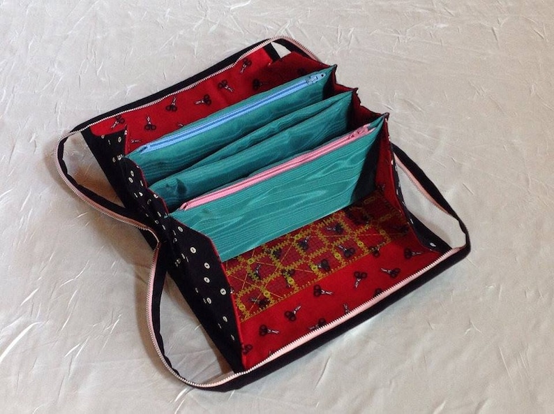 May include: A black zippered pouch with a pink zipper and a red, black, and gold patterned fabric lining. The pouch has four separate compartments with zippers.