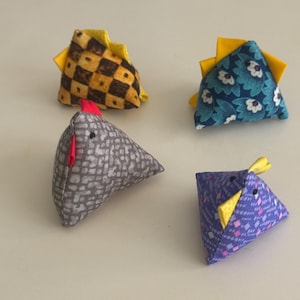 May include: Four handmade fabric chicken toys in various patterns and colors. One chicken is gray with a red comb, another is blue with white flowers, a third is purple with a geometric design, and the last is yellow and brown checkered.