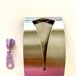 May include: A silver metal paper towel holder with a curved design. The holder has a slot for dispensing paper towels.
