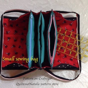 May include: A small sewing bag with three compartments, each with a zipper closure. The bag is made of black fabric with white polka dots and red fabric with a pattern of scissors. The bag is open and a yellow ruler is visible inside.