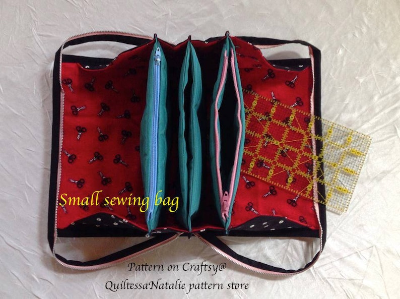 May include: A small sewing bag with three compartments, each with a zipper closure. The bag is made of black fabric with white polka dots and red fabric with a pattern of scissors. The bag is open and a yellow ruler is visible inside.