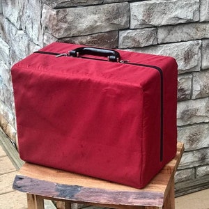 Può includere: Una custodia di trasporto rettangolare rossa con una maniglia nera. La custodia è realizzata in un materiale morbido e peluche e ha una chiusura a cerniera.