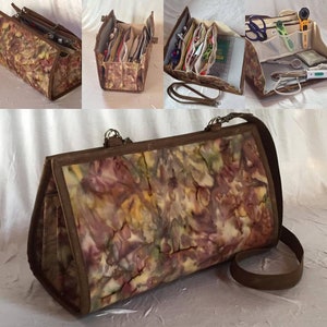 Pode incluir: Uma bolsa tote de tecido marrom com um padrão tie-dye multicolorido. A bolsa tem um fecho de correr e uma alça de ombro longa. A bolsa está aberta e mostra vários compartimentos no interior.