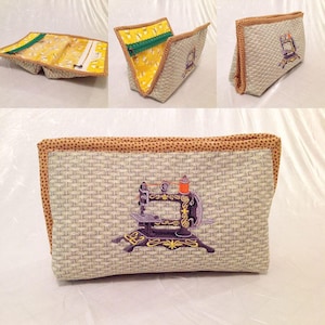 Può includere: Una pochette con cerniera in tessuto beige con un bordo marrone e una piccola immagine ricamata di una macchina da cucire vintage. La pochette è aperta per mostrare la fodera in tessuto giallo.