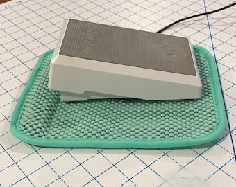 Non-slip pedal pad for sewing machine made of rubbery material reinforced with a thick lip to park the pedal