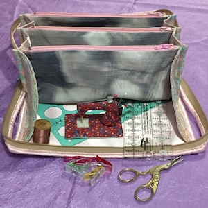 May include: A pink and gray fabric sewing kit with three zippered compartments, a small sewing machine, a spool of thread, a ruler, and a pair of scissors. The kit is open and the contents are visible.