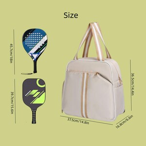 May include: A beige sports bag with white and tan stripes, measuring 37.5cm wide, 36.5cm high, and 16.8cm deep. Two pickleball paddles are shown, one blue and black, the other black and green. The bag has a zippered pocket.