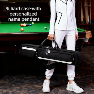 Op de afbeelding: Zwarte biljartkoffer met een gewatteerd ontwerp en witte accenten. De koffer heeft een handvat en een schouderriem. De tekst op de afbeelding luidt "Biljartkoffer met gepersonaliseerde naamhanger". Een gepersonaliseerde hanger hangt aan het handvat.