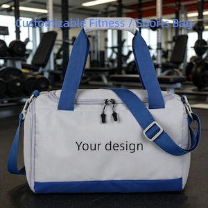 Könnte beinhalten: Eine weiße und blaue Sporttasche mit dem Text "Your design". Die Tasche hat einen blauen Griff und Schultergurt. Die Tasche befindet sich in einem Fitnessstudio mit Gewichten und Trainingsgeräten im Hintergrund. Der Text "Customizable Fitness / Sports Bag" steht oben.