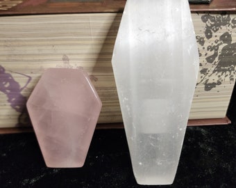 May include: Two coffin-shaped crystal carvings. One is a light pink rose quartz and the other is a white selenite.