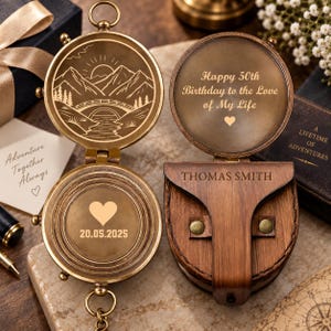 May include: A brass compass with a hinged lid featuring an engraved mountain and bridge scene. The interior lid reads Happy 50th Birthday to the Love of My Life with a heart. The base displays 20.05.2025 and a heart. A brown leather case is engraved THOMAS SMITH.