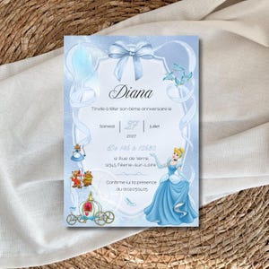 Peut inclure: Une invitation bleu clair avec un nœud et des illustrations de Cendrillon. La carte indique "Diana" et "Vous invite à fêter son anniversaire le samedi 27 juillet 2027."