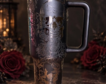 Puede incluir: Un vaso de acero inoxidable en color negro mate con un diseño grabado de calaveras y rosas. El recipiente cilíndrico y alto incluye un asa lateral resistente y una tapa de plástico negro con un mecanismo de cierre deslizante para bebidas.