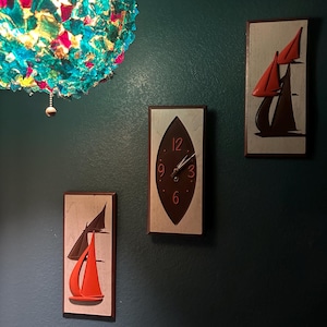 May include: Three wall decorations, a clock with a brown face and white numbers, and two sailboats with red sails on a white background.