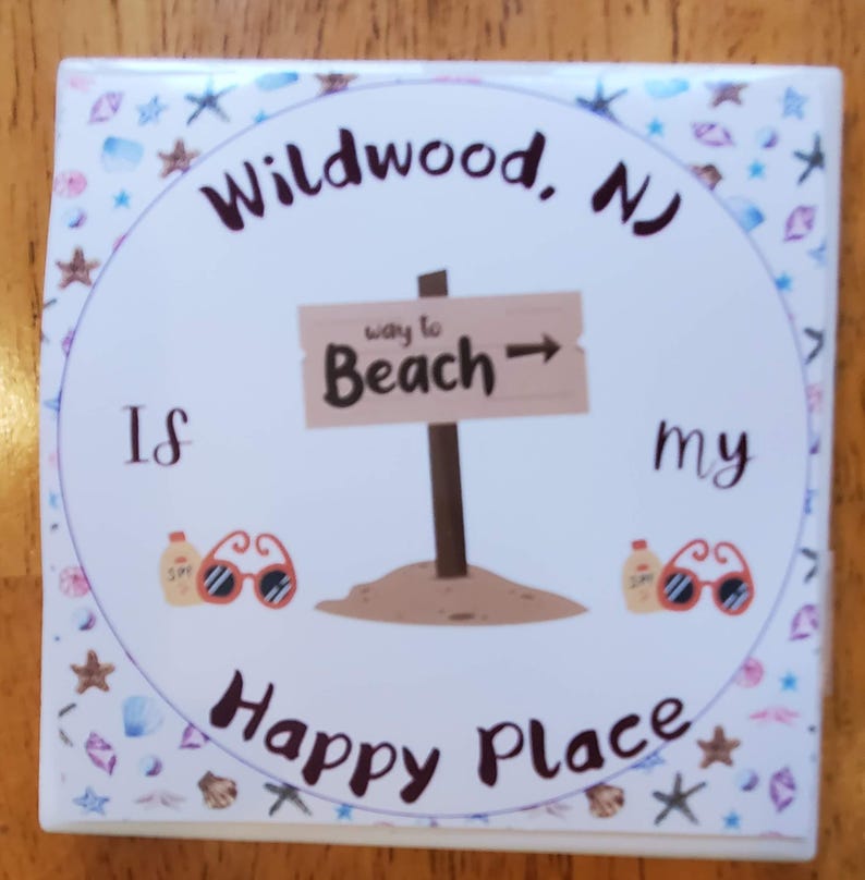 K&ouml;nnte beinhalten: Wei&szlig;er Keramikuntersetzer mit einem bunten Rand aus Muscheln und Sternen. Der Untersetzer zeigt den Text "Wildwood, NJ is my happy place" mit einem braunen Holzschild, das nach rechts zeigt und "way to Beach" sagt.