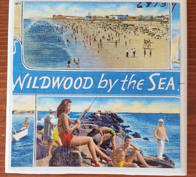May include: A vintage postcard featuring a beach scene with the text "WILDWOOD by the SEA." The postcard shows a beach with people swimming and sunbathing, and a boardwalk in the background. The postcard is in good condition, with some minor wear and tear.