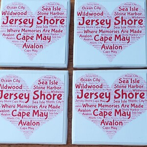 K&ouml;nnte beinhalten: Vier wei&szlig;e Keramikuntersetzer mit herzf&ouml;rmigem Design. Das Design zeigt die W&ouml;rter "Jersey Shore", "Cape May" und andere K&uuml;stenstadtnamen in roter Schrift, wodurch ein Collage-Effekt entsteht.