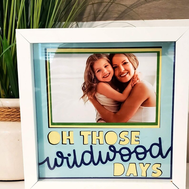 May include: White framed photo with a picture of a woman and a young girl hugging. The photo is set against a light blue background with the words "OH THOSE wildwood DAYS" in yellow and blue lettering.