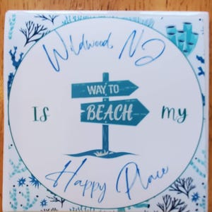 May include: White ceramic coaster with a blue and white design. The coaster features a sign that says "Way to Beach" and the text "Wildwood, NJ is my happy place".