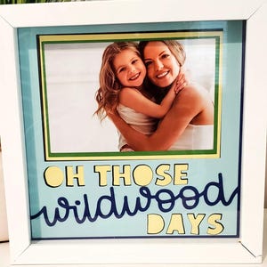 May include: White framed photo with a picture of a woman and a child hugging. The photo is surrounded by a light blue background with the words "OH THOSE wildwood DAYS" in yellow and dark blue lettering.