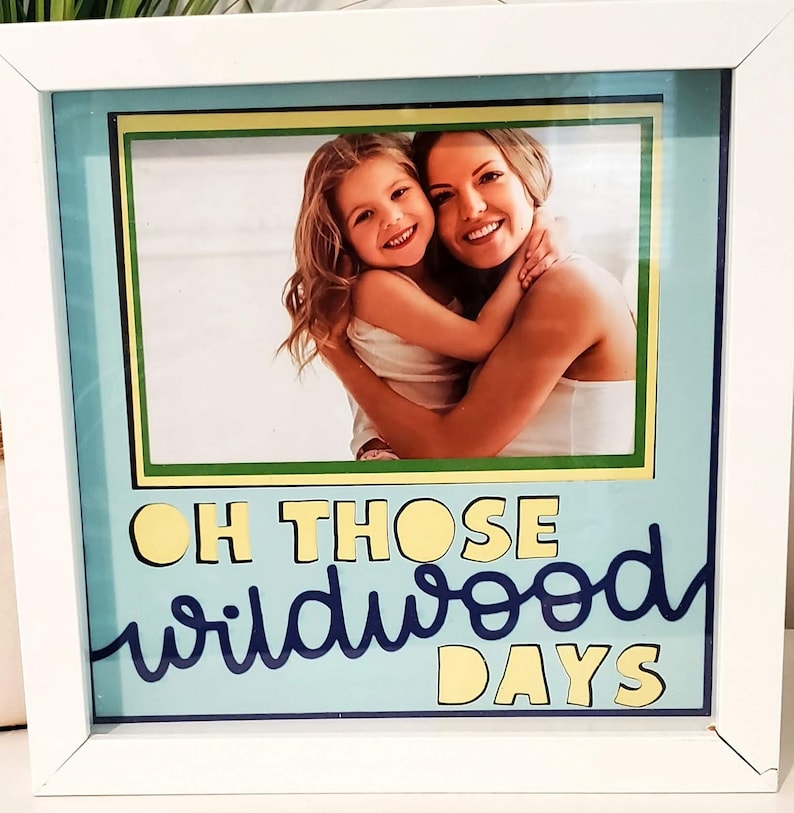 May include: White framed photo with a picture of a woman and a child hugging. The photo is surrounded by a light blue background with the words "OH THOSE wildwood DAYS" in yellow and dark blue lettering.