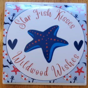 K&ouml;nnte beinhalten: Ein wei&szlig;er Keramikuntersetzer mit einem blauen und roten Seestern-Design. Der Untersetzer hat einen blauen und wei&szlig;en nautischen Musterrand und den Text "Star Fish Kisses Wildwood Wishes".