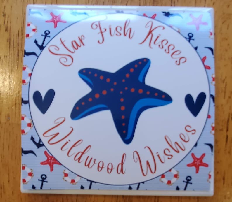 K&ouml;nnte beinhalten: Ein wei&szlig;er Keramikuntersetzer mit einem blauen und roten Seestern-Design. Der Untersetzer hat einen blauen und wei&szlig;en nautischen Musterrand und den Text "Star Fish Kisses Wildwood Wishes".